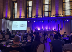 People sit at tables while watching a presenter showing a slide deck. 